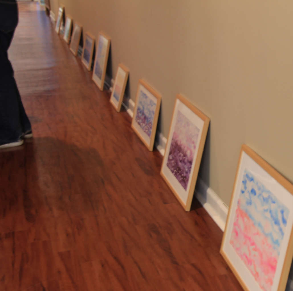 Colorful Horizons framed horizon watercolor landscape paintings, leaning on gallery wall before installation for artist's solo art show; Getting Ready painting third from lower right