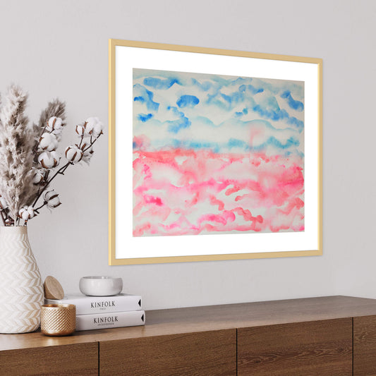 Framed pink and blue Cotton Candy horizon landscape watercolor above table with books and vase
