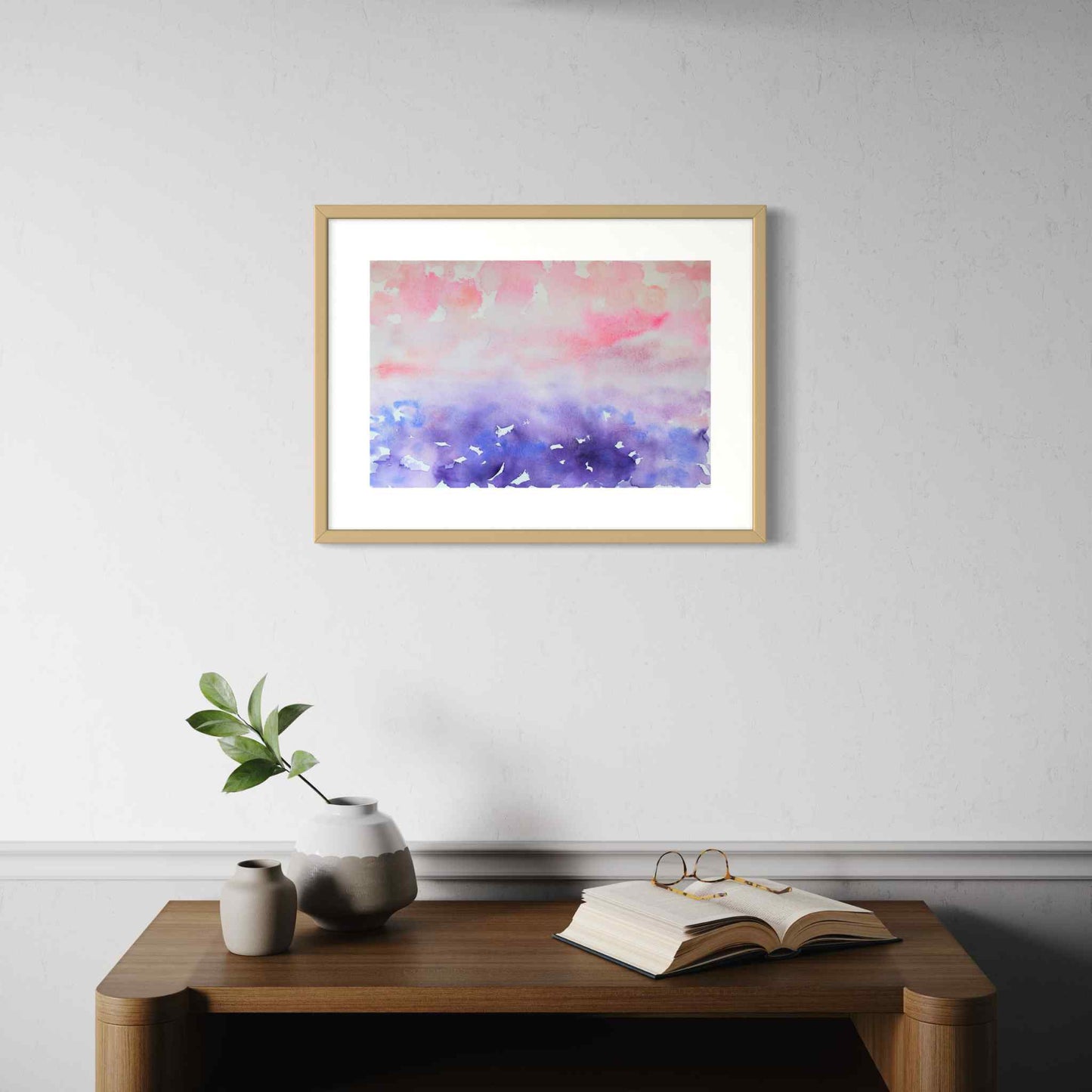 Happy Mist pink and purple watercolor horizon, framed, above wooden side table