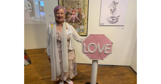Woman standing next to a pink 'LOVE' sign sculpture in an art gallery