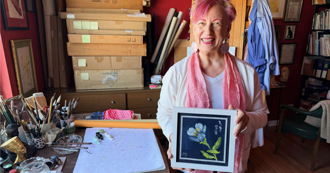 Woman in her art studio holding white flower painting on navy blue paper in art studio