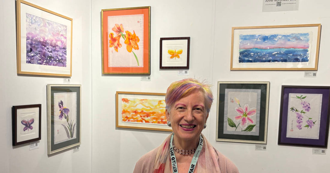 Artist standing in front of her framed paintings at an art exhibition