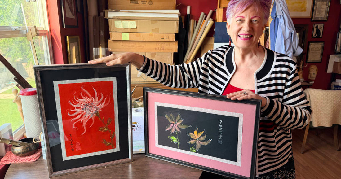 Woman in art studio holding two colorful framed flower paintings