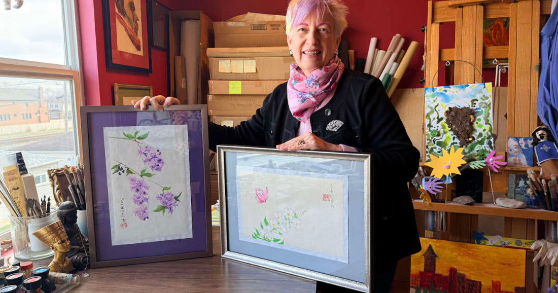 Woman holding two framed artworks in an art studio.