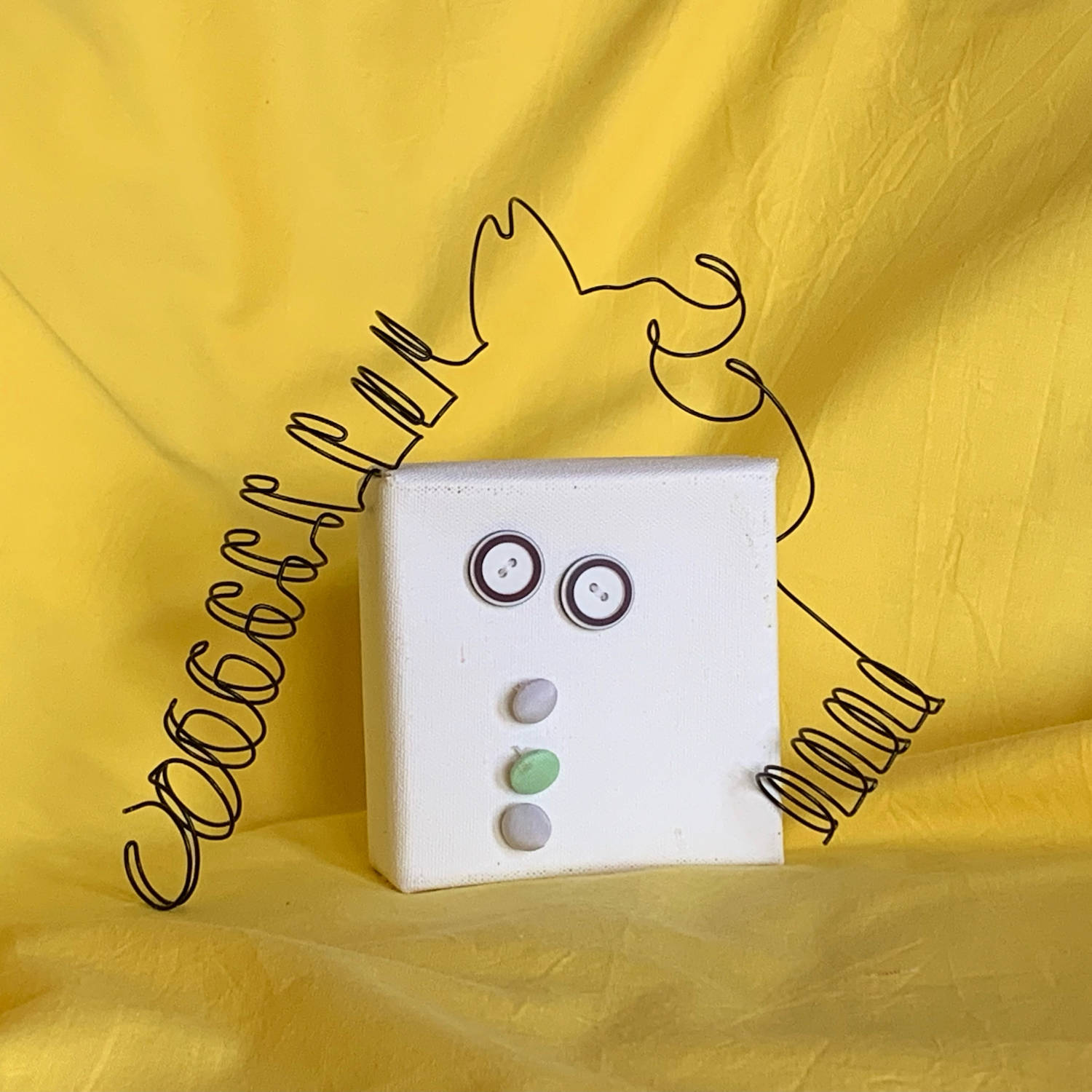 Whimsical mixed media portrait sculpture-white square canvas head, buttons for eyes, black spiral wire hair, with bright yellow background