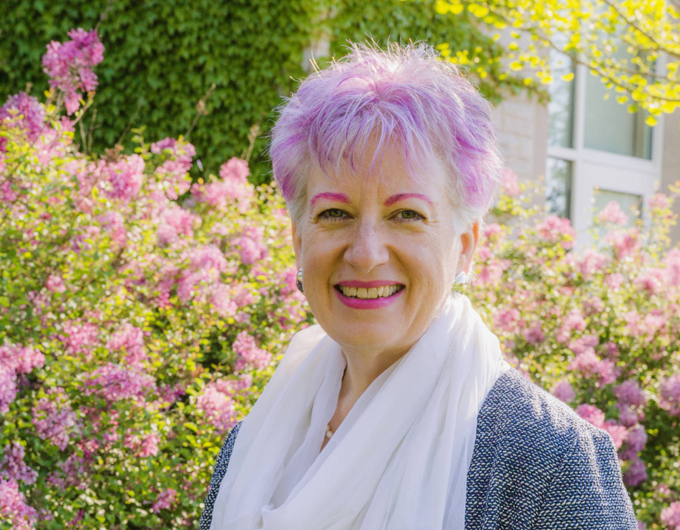 Artist Anne Nordhaus-Bike, pink eyebrows/lipstick, purple hair, outdoors, sunny day, pink flowers 