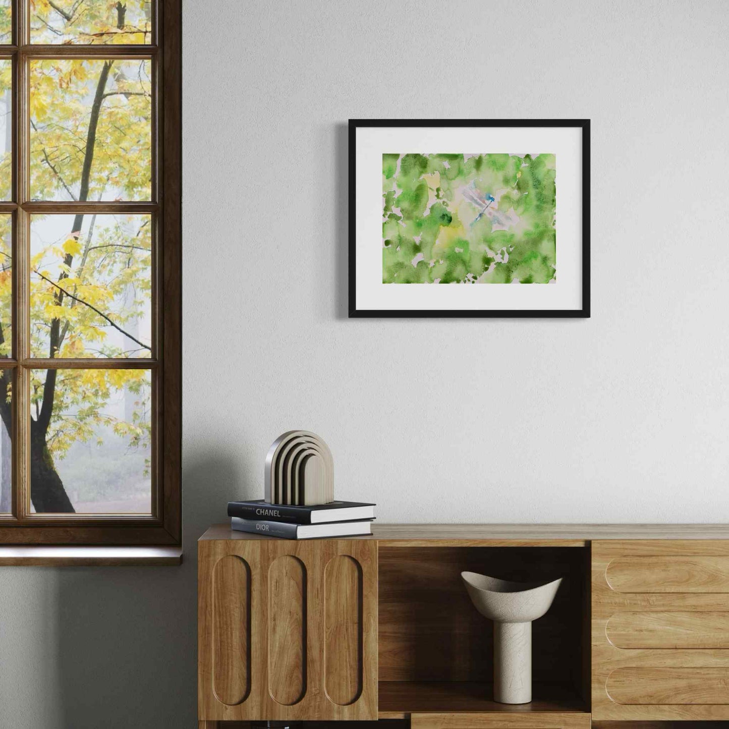 Silvery dragonfly in green garden framed watercolor painting, above credenza next to sunny window
